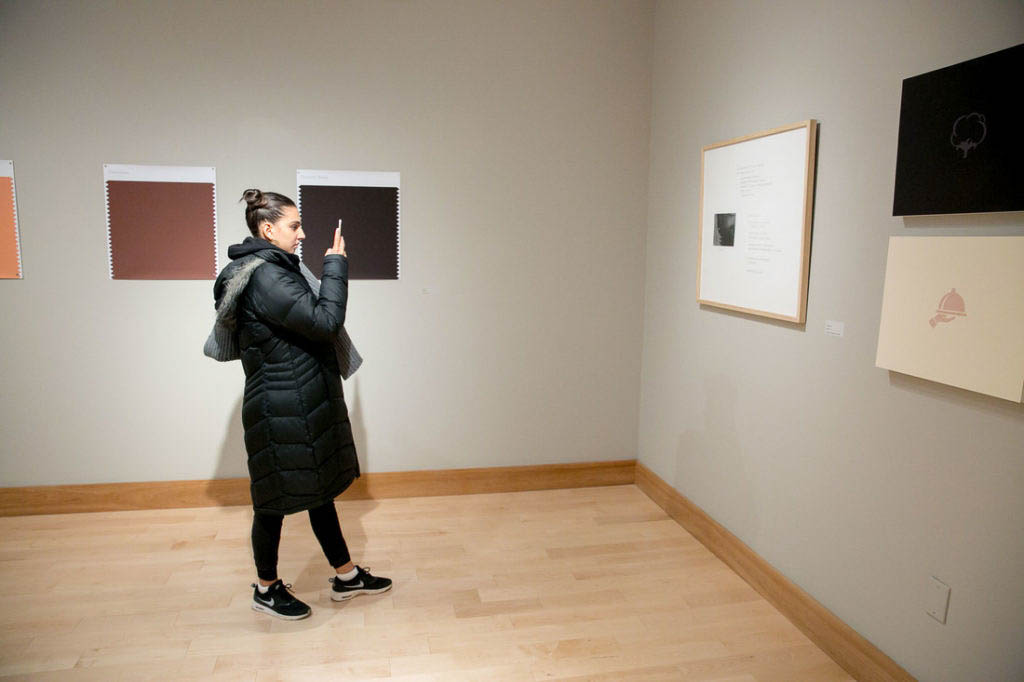 One person taking a photo with their cellphone of a wall piece in the gallery